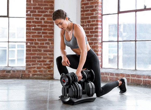 Female model using the BowFlex Adjustable Dumbell in a fitness studio