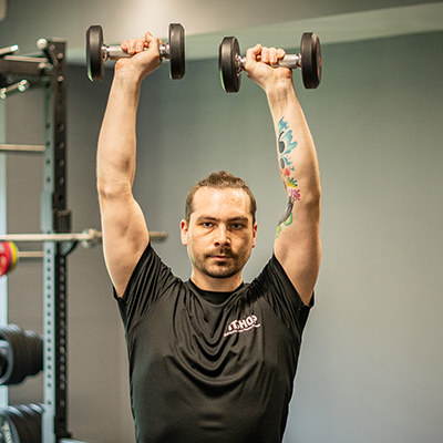 model performing a shoulder press with dumbbells. 