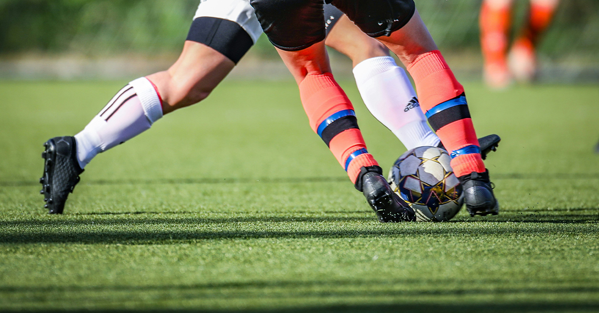 A dynamic photograph of two football players handling the football. The photograph is at knee height.