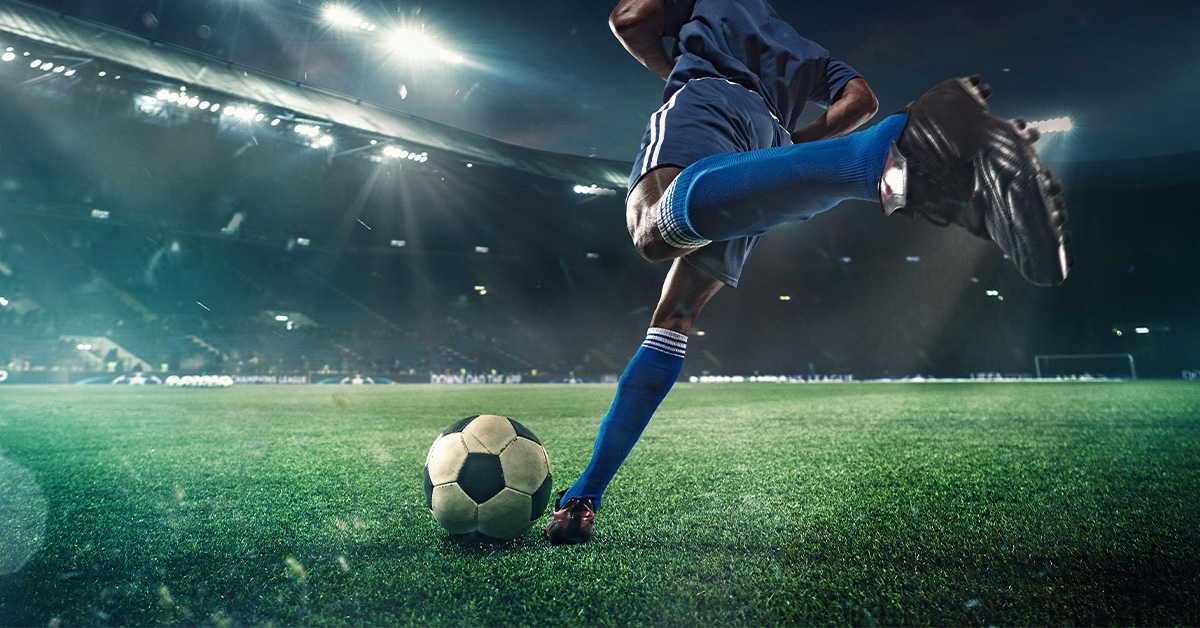 A footballer about to kick a soccer ball in a stadium.