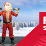 Model dressed as Santa Claus lifting dumbbells on a gym mat with a snowy winter landscape in the background, alongside a red graphic panel showing the Fitshop logo.