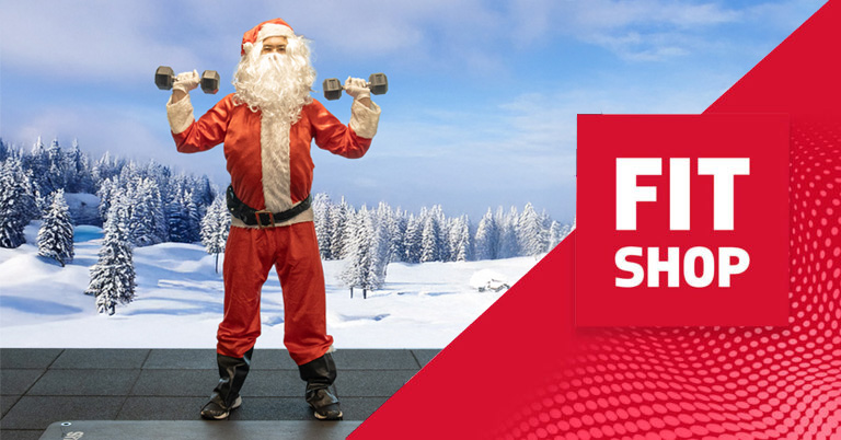 Model dressed as Santa Claus lifting dumbbells on a gym mat with a snowy winter landscape in the background, alongside a red graphic panel showing the Fitshop logo.